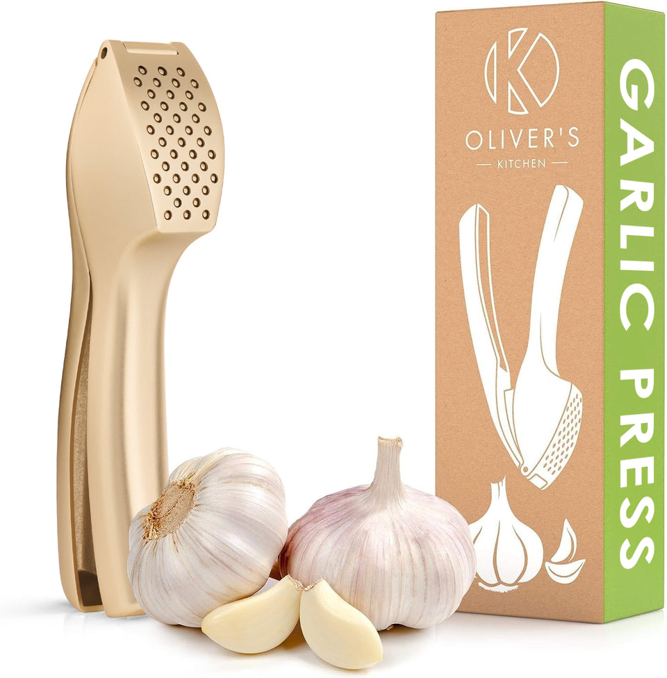 Garlic press in matt gold with its kraft card gift box and fresh garlic bulbs